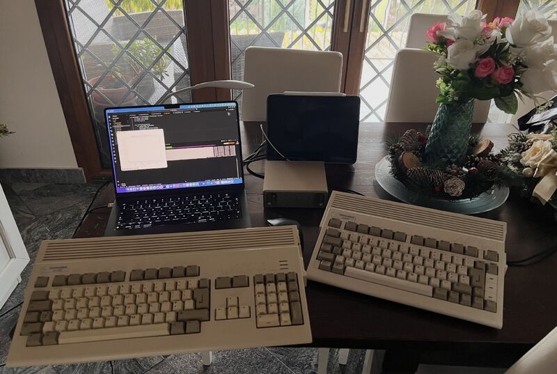 Due computer Amiga sul tavolo, davanti a un portatile e ad altri dispositivi moderni.